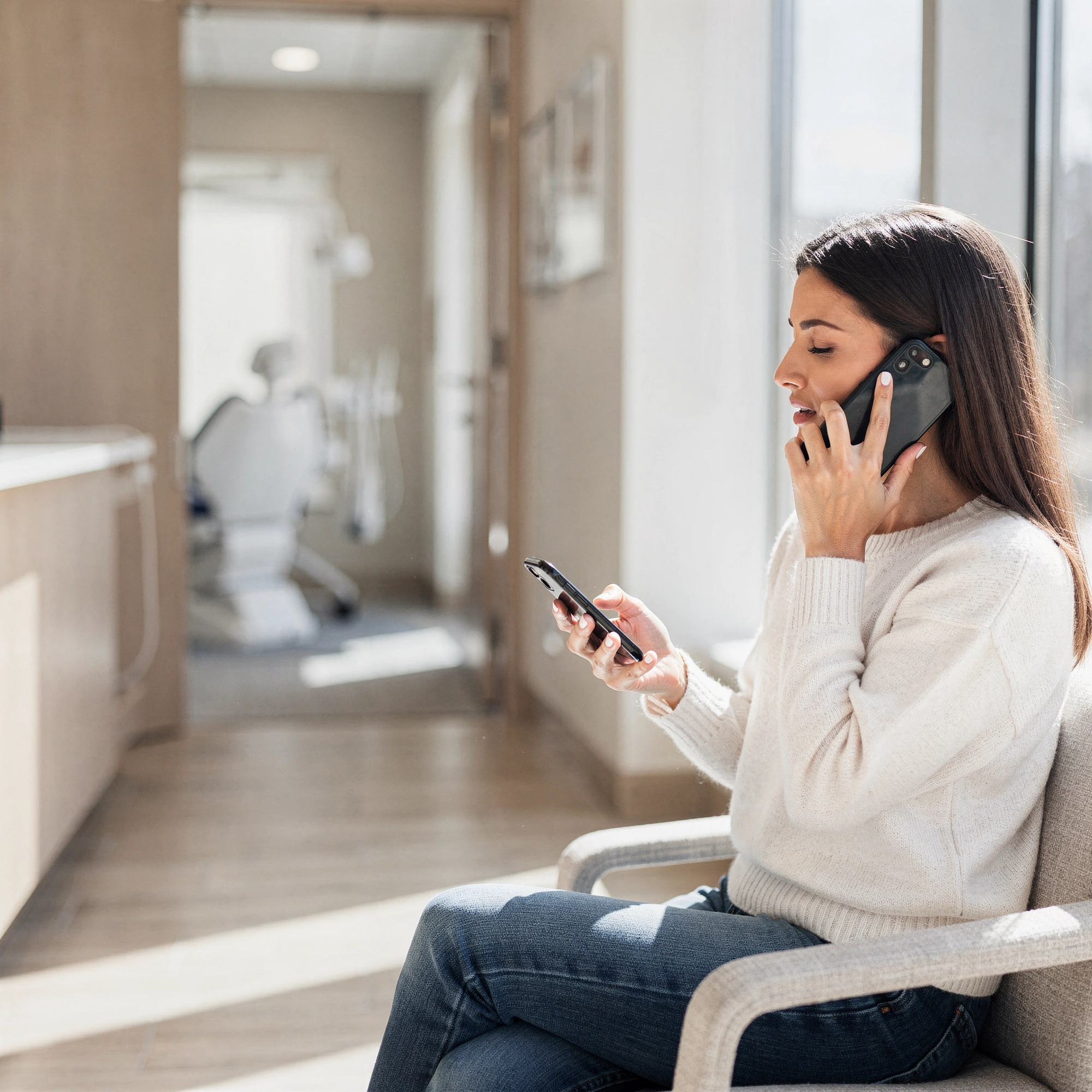 Woman on phone in dental office waiting area with treatment room visible in background